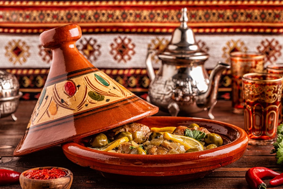 tajine poulet citron et olives dans un plat traditionnel marocain avec un berrad et des gobelets en verre sur une table en bois